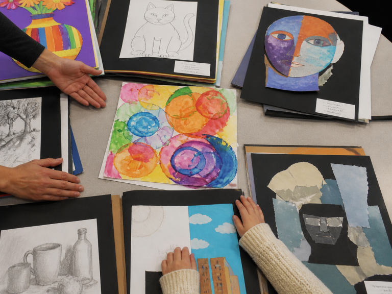 artwork review Colorful art pieces laid out on a table with hands examining them.