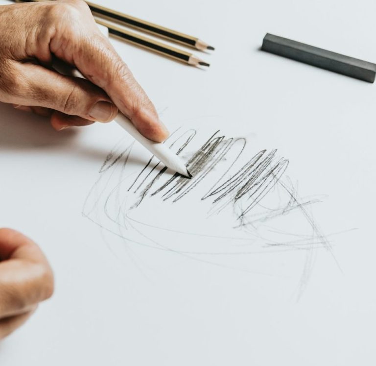 Drawing A person’s hands sketching with a pencil and colored pencils on white paper.