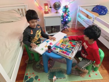 Two boys sit at a table in a colorful room, engaged in creative activities with toys.