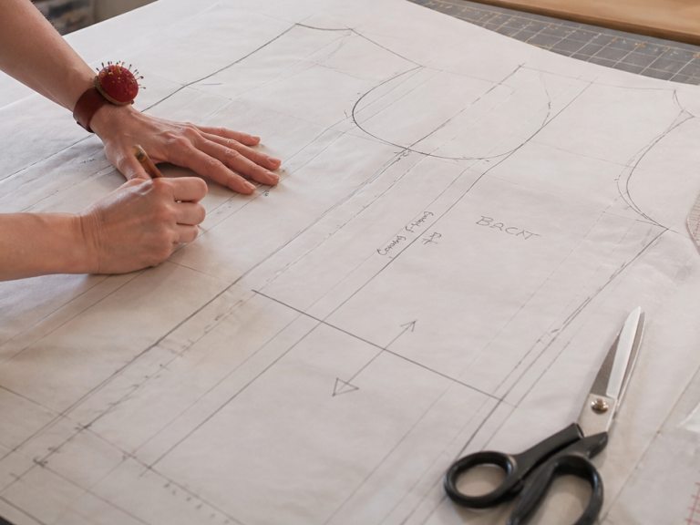pattern making A person sketches sewing patterns on paper with a sewing machine in the background.